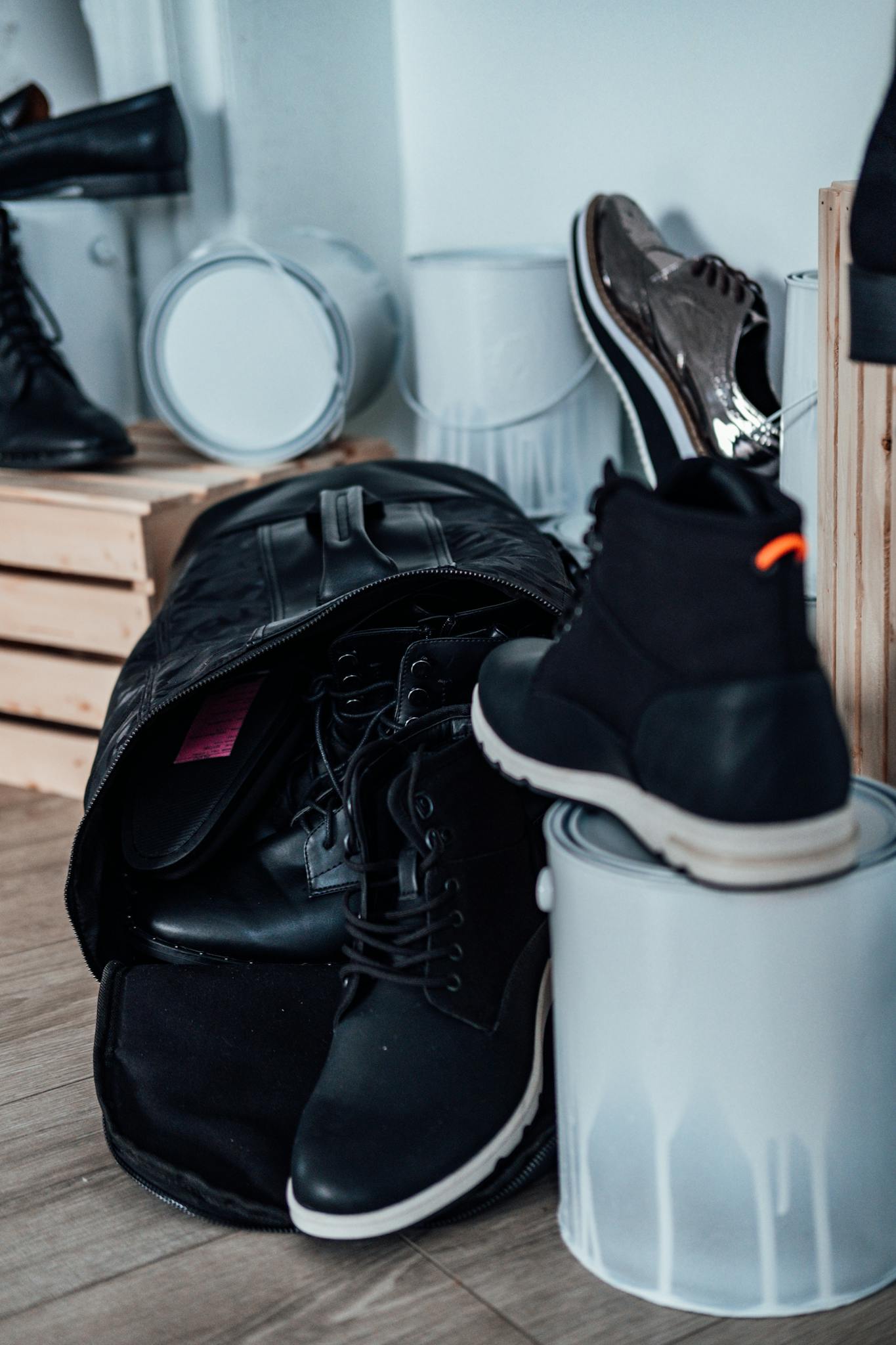 A stylish display of black boots and a backpack among paint cans indoors, showcasing modern casual fashion.