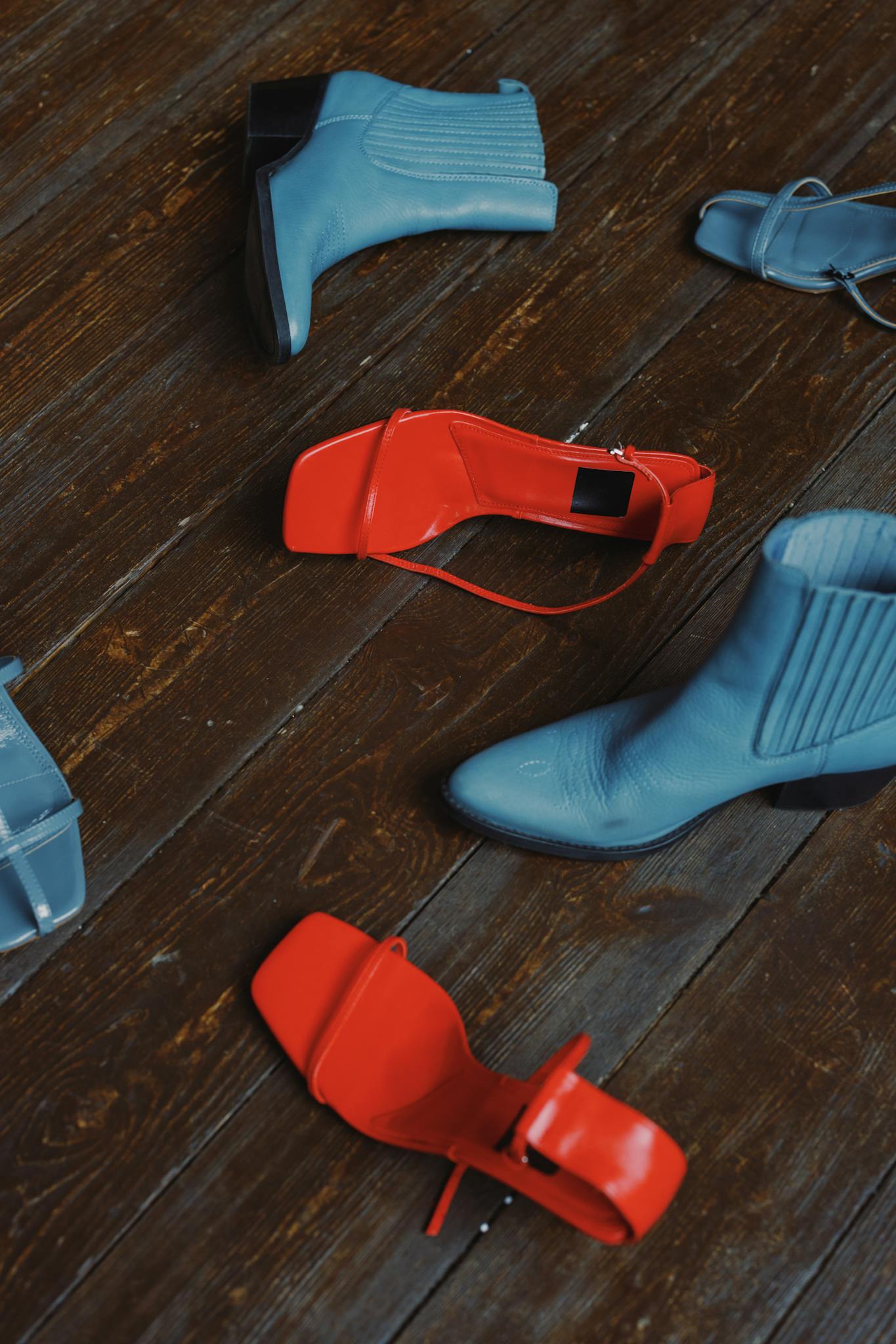 Close-up view of blue boots and red sandals on rustic wooden planks.